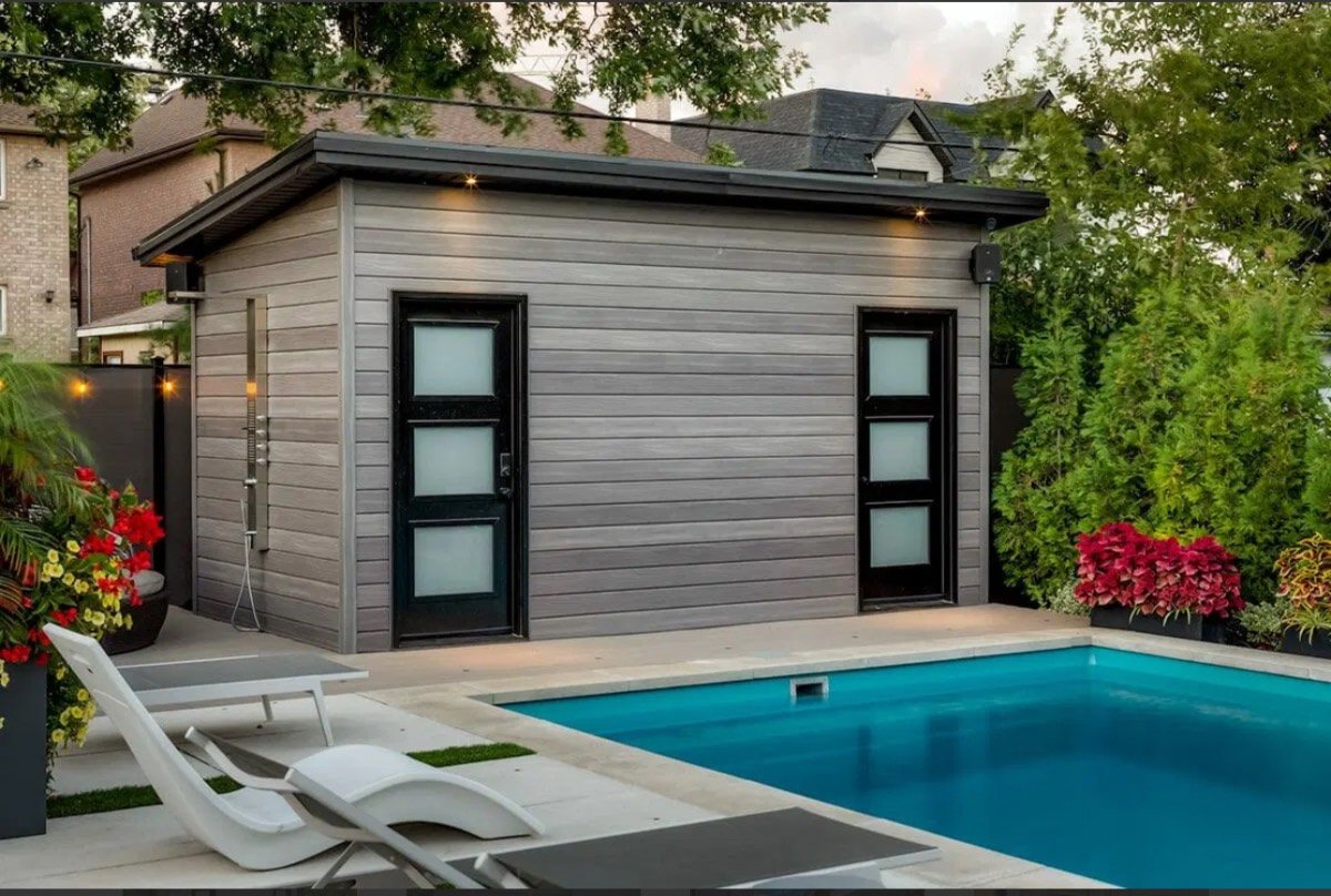 Modern composite-clad pool cabana lit at dusk beside a swimming pool